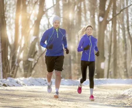 Junges Paar joggt durch verschneiten Wald in Sportkleidung &ndash; Bewegung und Ausdauertraining als Teil eines gesunden Lebensstils.