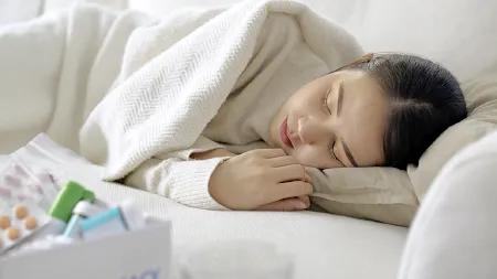 Frau liegt krank auf dem Sofa, in eine Decke gehüllt – Symbolbild für Ruhe und Genesung bei Erkältung.