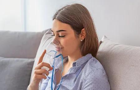 Junge Frau mit Inhalationsmaske sitzt entspannt auf dem Sofa – Inhalation zur Linderung von Atemwegserkrankungen