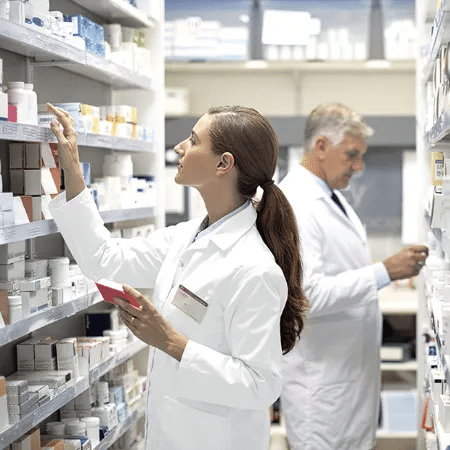 Zwei Apotheker:innen in wei&szlig;em Kittel sortieren Medikamente in der Sichtwahl der Apotheke