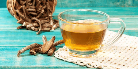 Tasse mit Baldriantee und getrockneten Wurzeln auf türkisem Untergrund