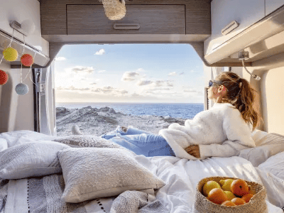 Frau liegt entspannt in einem gem&uuml;tlichen Campervan mit Blick auf das Meer