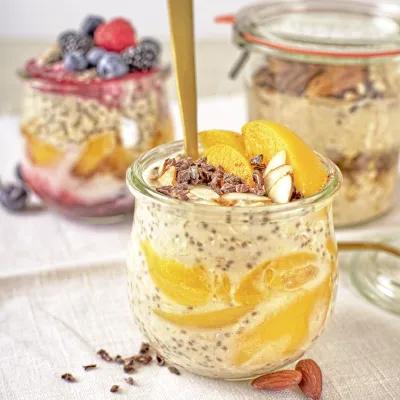 Chia-Kokos-Müsli mit Mango und Mandeln in einem Glas, im Hintergrund zwei weitere Müsligläser.