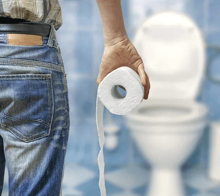 Ein Mensch in Jeans steht vor einer Toilette und h&auml;lt eine Rolle Toilettenpapier locker in der Hand &ndash; Symbolbild f&uuml;r Darmbeschwerden oder Verdauungsprobleme.