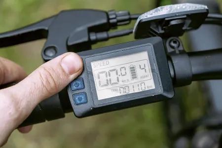 Nahaufnahme eines Fahrradcomputers mit digitalem Display, auf dem Geschwindigkeit und zur&uuml;ckgelegte Strecke angezeigt werden, w&auml;hrend ein Finger eine Taste dr&uuml;ckt.