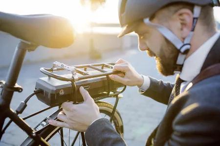 Mann mit Fahrradhelm installiert oder entfernt einen Akku von einem E-Bike bei Sonnenaufgang oder -untergang.