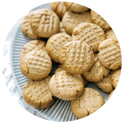 Runde Erdnusskekse mit Gabelmuster auf einem geriffelten Teller &ndash; klassische Pl&auml;tzchen mit Erdnussgeschmack.