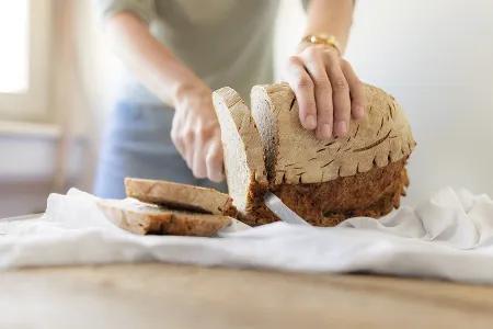 Eine Person schneidet mehrere Scheiben Brot von einem Laib auf einem weißen Tuch.