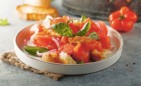 Ein Teller mit frischem Tomatensalat, roten Zwiebeln, Basilikum und knusprigem Brot steht auf einem gedeckten Tisch – Sinnbild für herzgesunde Ernährung.
