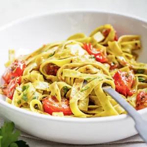 Pasta mit frischen Tomatenst&uuml;cken, Pesto und Kr&auml;utern in einer wei&szlig;en Schale.
