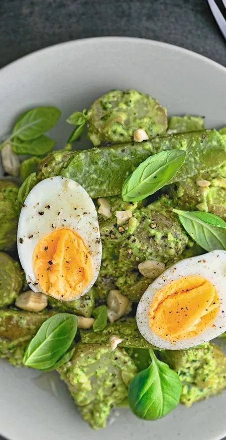 Kartoffelravioli mit gr&uuml;nem Pesto, Basilikumbl&auml;ttern und halbiertem Ei auf einem wei&szlig;en Teller