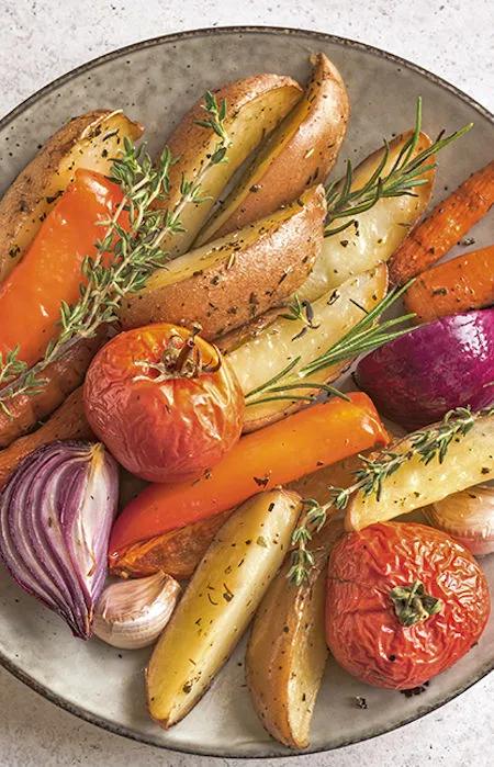 Ofengem&uuml;se mit Kartoffeln, Karotten, Tomaten, Zwiebeln und Kr&auml;utern auf einem rustikalen Teller