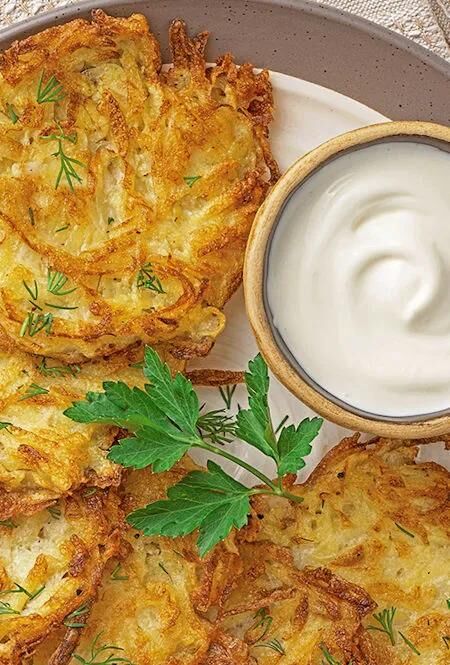 Frisch gebratene Kartoffelpuffer mit Sahnedip, serviert mit Petersilie auf einem hellen Teller