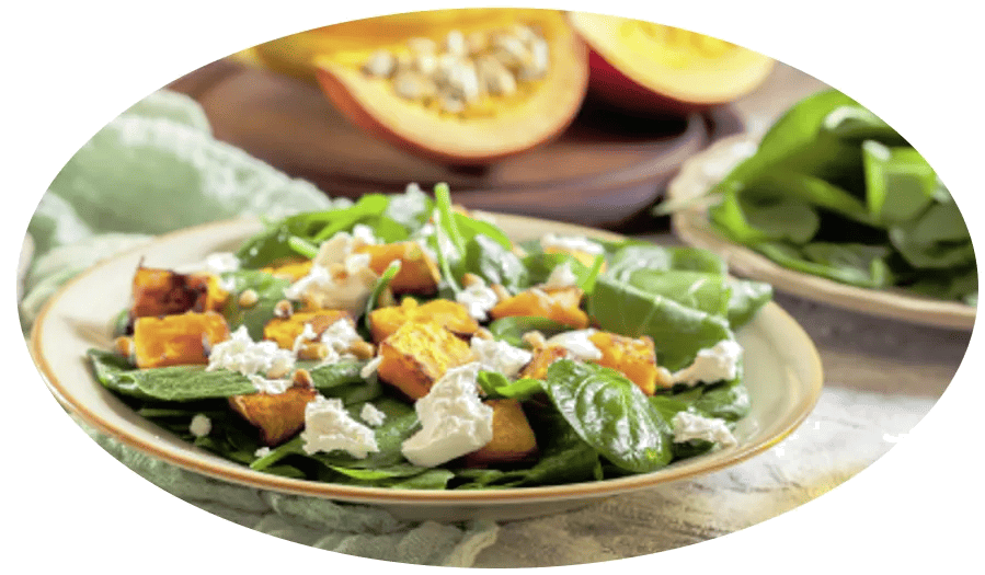 Kürbissalat mit gebratenem Kürbis, frischem Spinat und Feta auf einem Teller, im Hintergrund ein aufgeschnittener Kürbis.