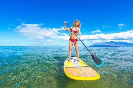 Frau in rotem Bikini paddelt auf einem gelben Stand-Up-Paddle-Board auf ruhigem, klarem Meer bei sonnigem Wetter.