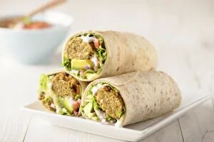 Drei aufgeschnittene Wraps gefüllt mit Falafel, Avocado, Gemüse und Joghurt-Dressing, auf einem weißen Teller.