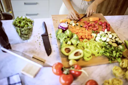 Eine Person schneidet auf einem Küchentresen frisches Gemüse wie Avocados, Karotten, Tomaten und Paprika – Symbol für reizdarmfreundliche Ernährung.