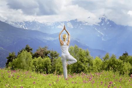 Frau macht Yoga auf einer Blumenwiese mit Blick auf Berge