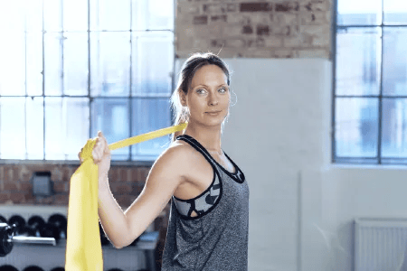 Frau mit Fitnessband beim Schultertraining im Fitnessstudio