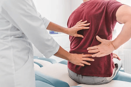 Ärztin oder Physiotherapeutin untersucht unteren Rücken eines Mannes