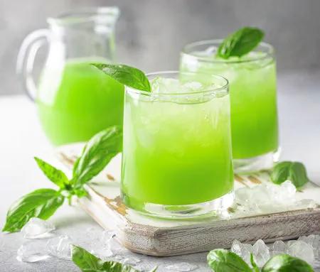Sommerliches Getränk mit grüner Farbe und Basilikum, serviert auf Eis in einem Glas
