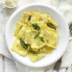 Ravioli mit Salbeibl&auml;ttern und geriebenem Parmesan auf wei&szlig;em Teller.