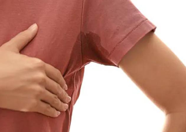 Nahaufnahme eines Oberk&ouml;rpers mit einem roten T-Shirt, das unter der Achsel deutlich sichtbar vom Schwei&szlig; durchtr&auml;nkt ist. Eine Hand h&auml;lt den Arm leicht an.