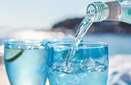 Frisches Mineralwasser wird an einem sonnigen Tag in ein Glas mit Eiswürfeln und Limette gegossen.