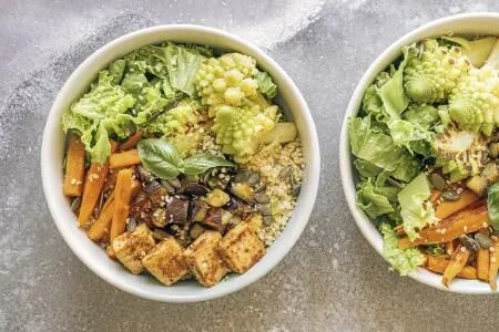 Gesunde Bowl mit Romanesco, Salat, M&ouml;hren, Tofu und K&ouml;rnern auf heller Oberfl&auml;che