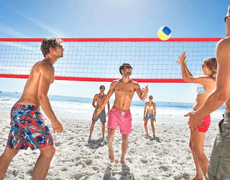 Gruppe junger Erwachsener spielt Beachvolleyball am sonnigen Sandstrand.