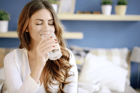 Junge Frau trinkt ein Glas Wasser &ndash; Symbolbild f&uuml;r gesunde Vaginalflora durch ausreichende Fl&uuml;ssigkeitszufuhr.