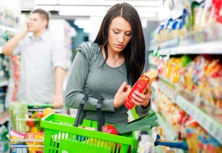Frau beim Einkaufen im Supermarkt, pr&uuml;ft konzentriert die Inhaltsstoffe eines Produkts &ndash; bewusstes Konsumverhalten bei veganer Ern&auml;hrung.