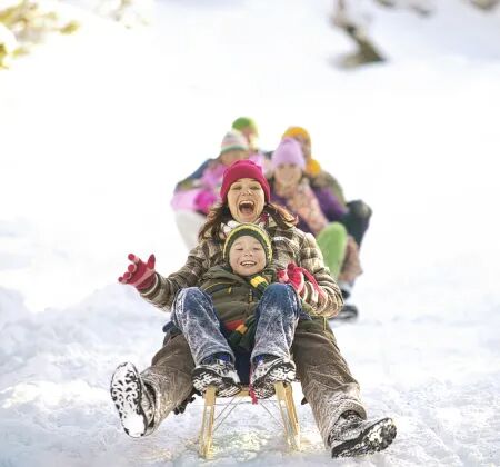 Familie mit Kind fährt lachend auf einem Holzschlitten durch den Schnee, Spaß im Winterwunderland.